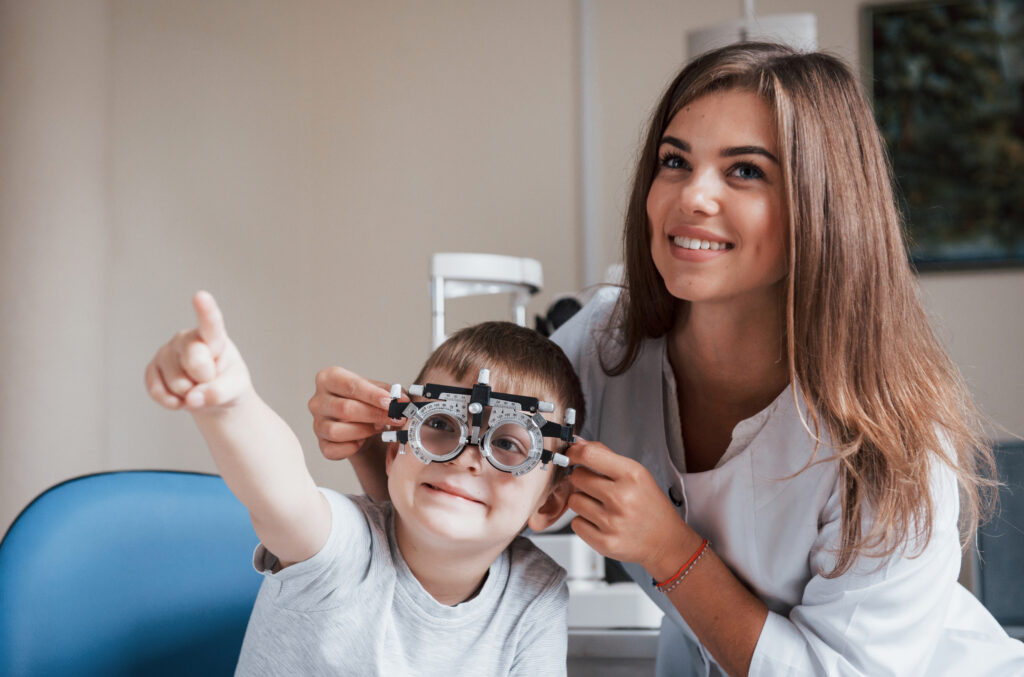 criança em consulta de oftalmologia com óculos de teste de graduação a apontar enquanto a médica oftalmologista o ajuda